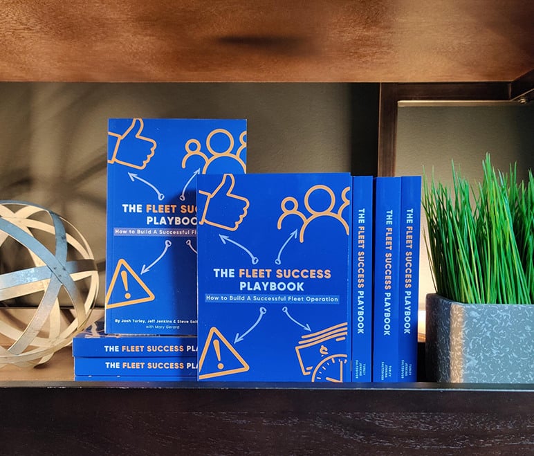 Copies of The Fleet Success Playbook stacked on a shelf